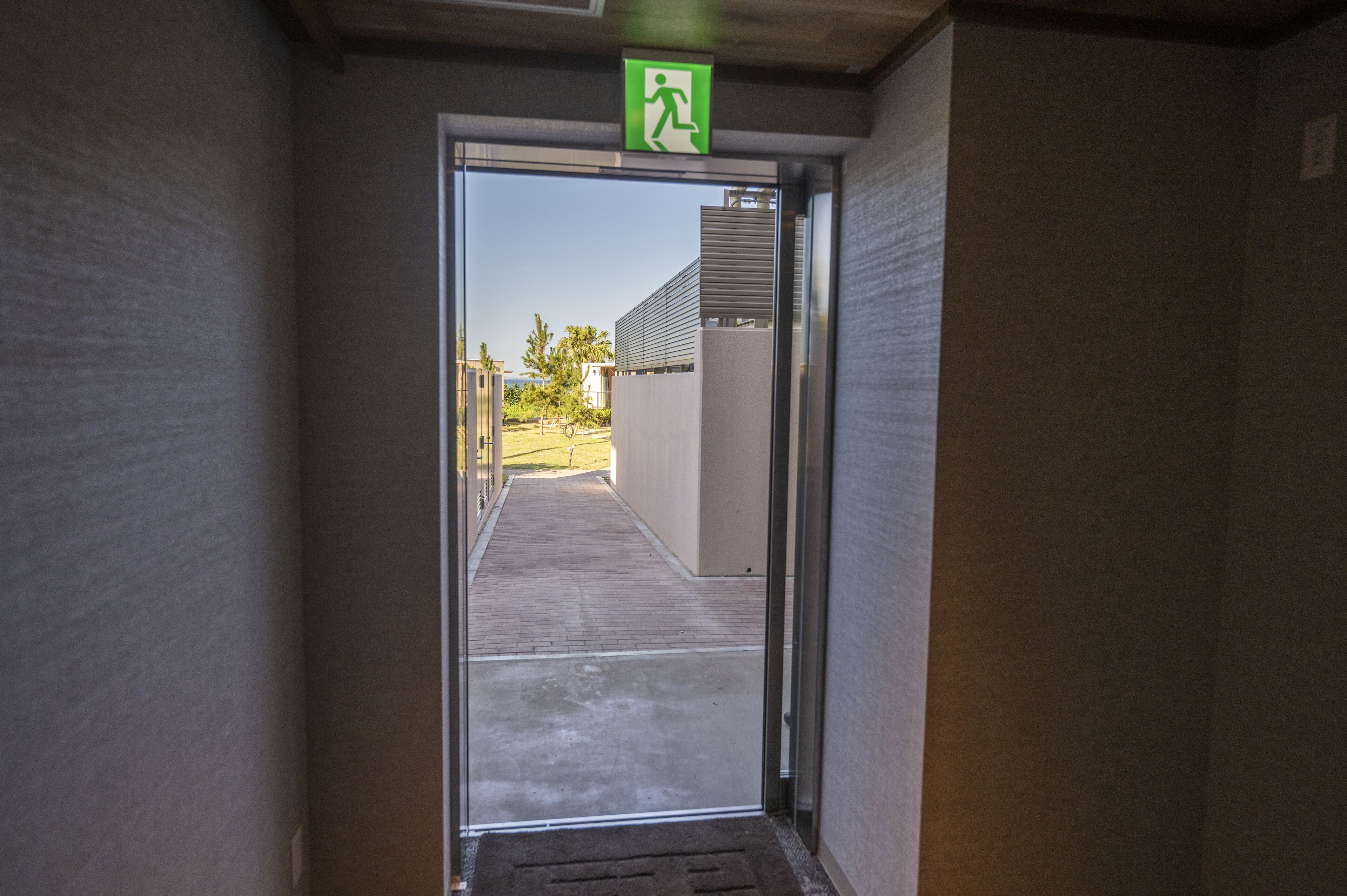 A hallway leading to a glass door with an emergency exit sign.