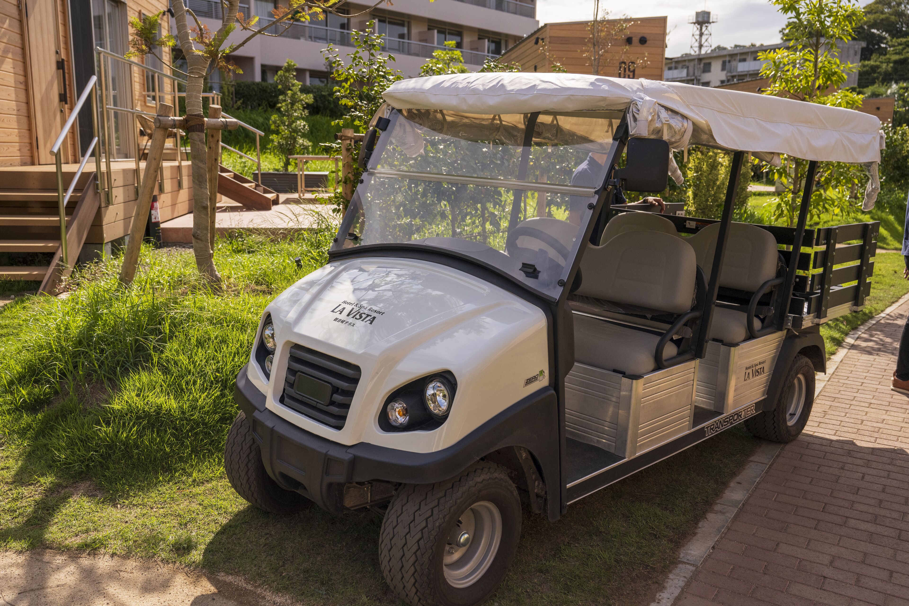 Ein Golfmobil steht auf einem befestigten Weg, im Hintergrund sind ein Holzbau und Grünflächen zu sehen.