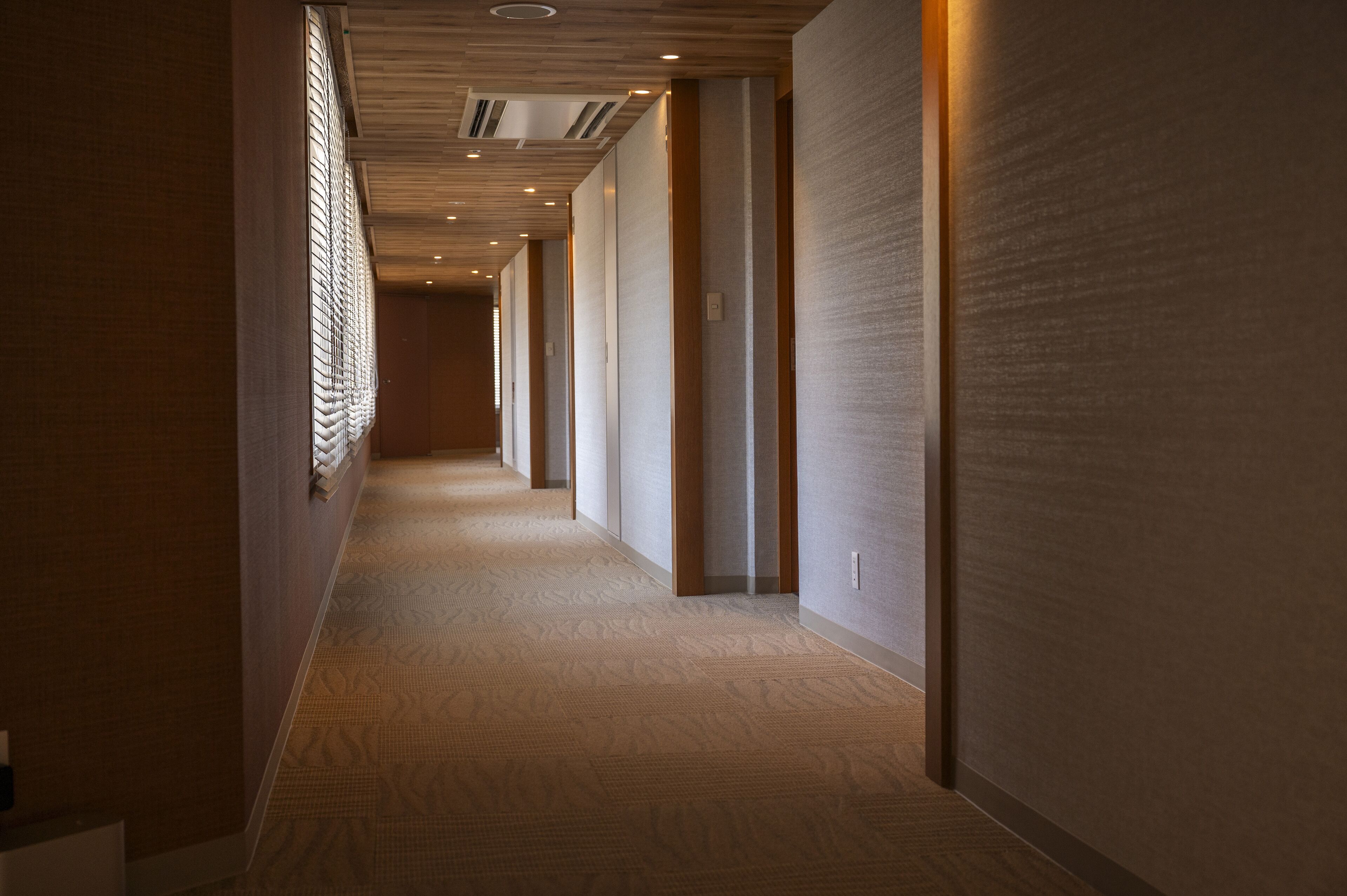 A long, narrow hallway with patterned carpet, wooden paneling on the walls, and recessed lighting.