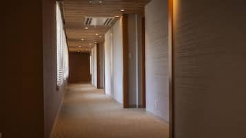 A long, narrow hallway with patterned carpet, wooden paneling on the walls, and recessed lighting.