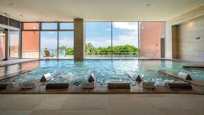 An indoor swimming pool with clear glass walls, a view of greenery outside, and a modern interior design.