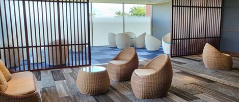 A modern lounge area with wicker furniture, a patterned carpet, and a view through a glass partition to the outdoors.