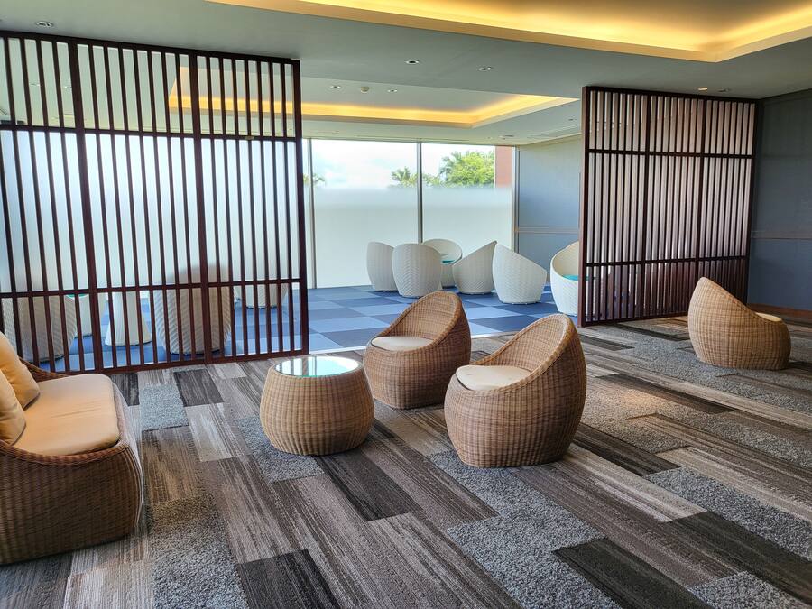 A modern lounge area with wicker furniture, a patterned carpet, and a view through a glass partition to the outdoors.