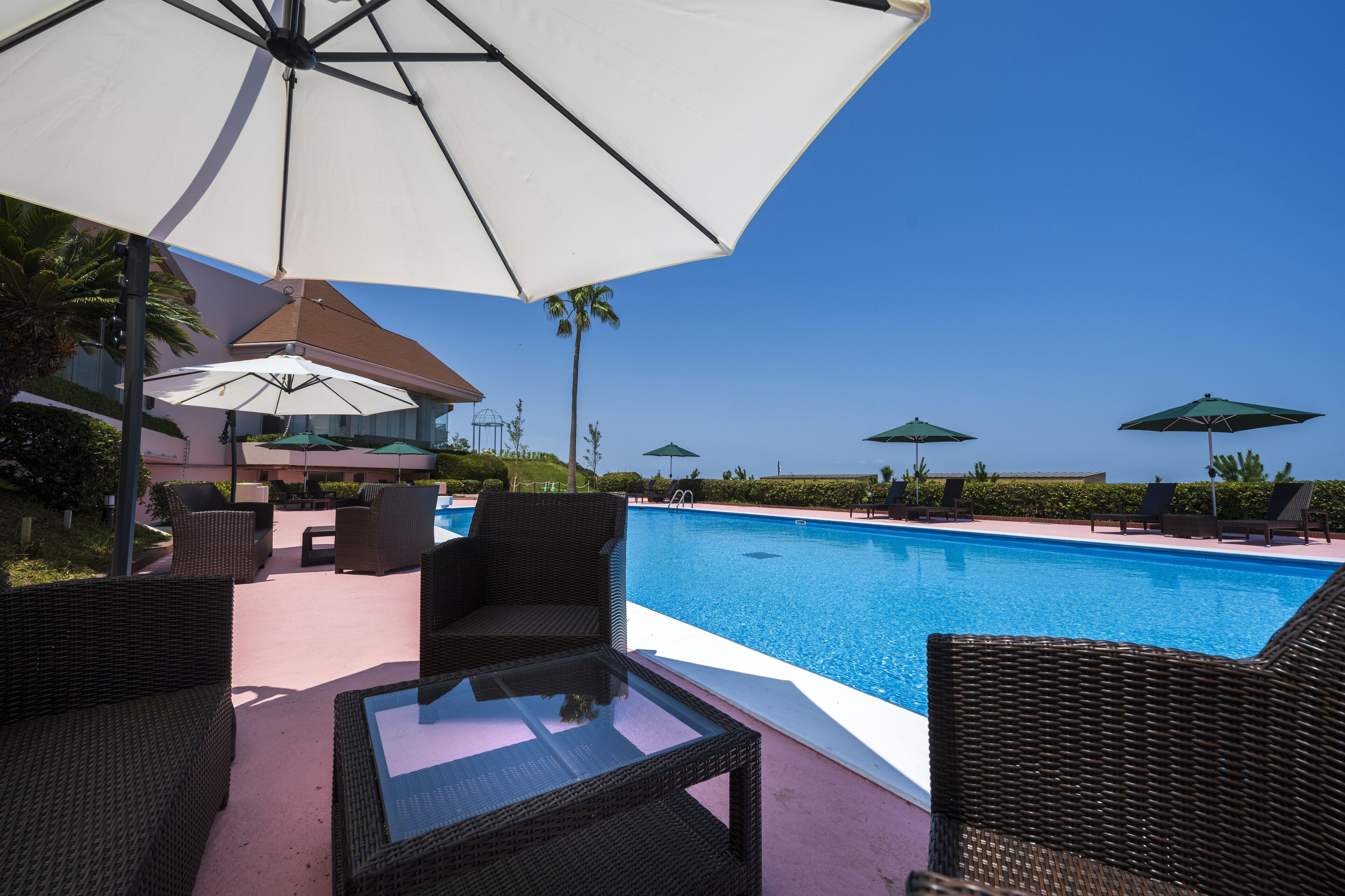 A poolside area with wicker furniture and umbrellas, a clear blue sky, and a pool.
