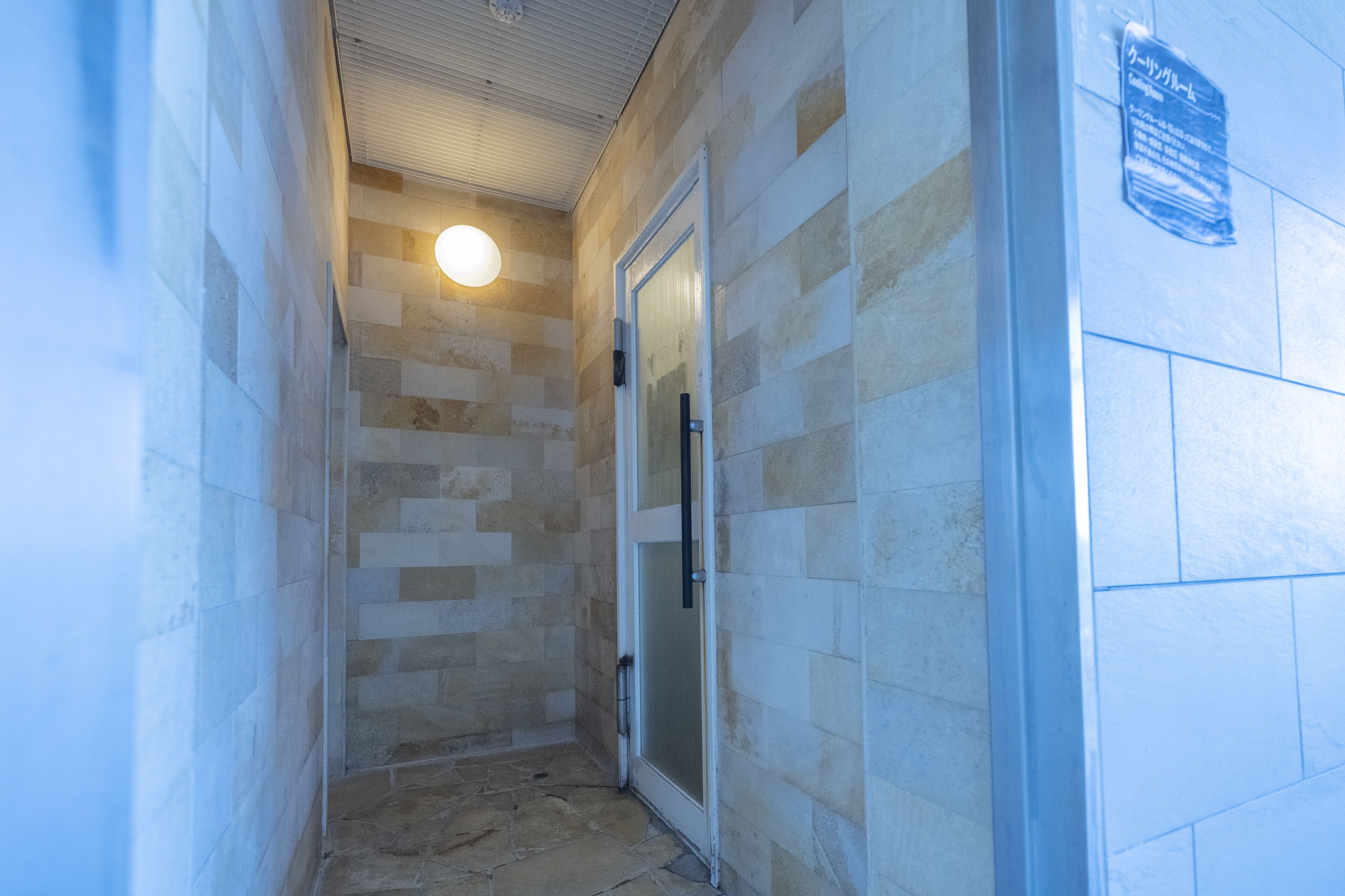 Un pasillo estrecho con paredes de piedra y una puerta de cristal que da a una habitación.