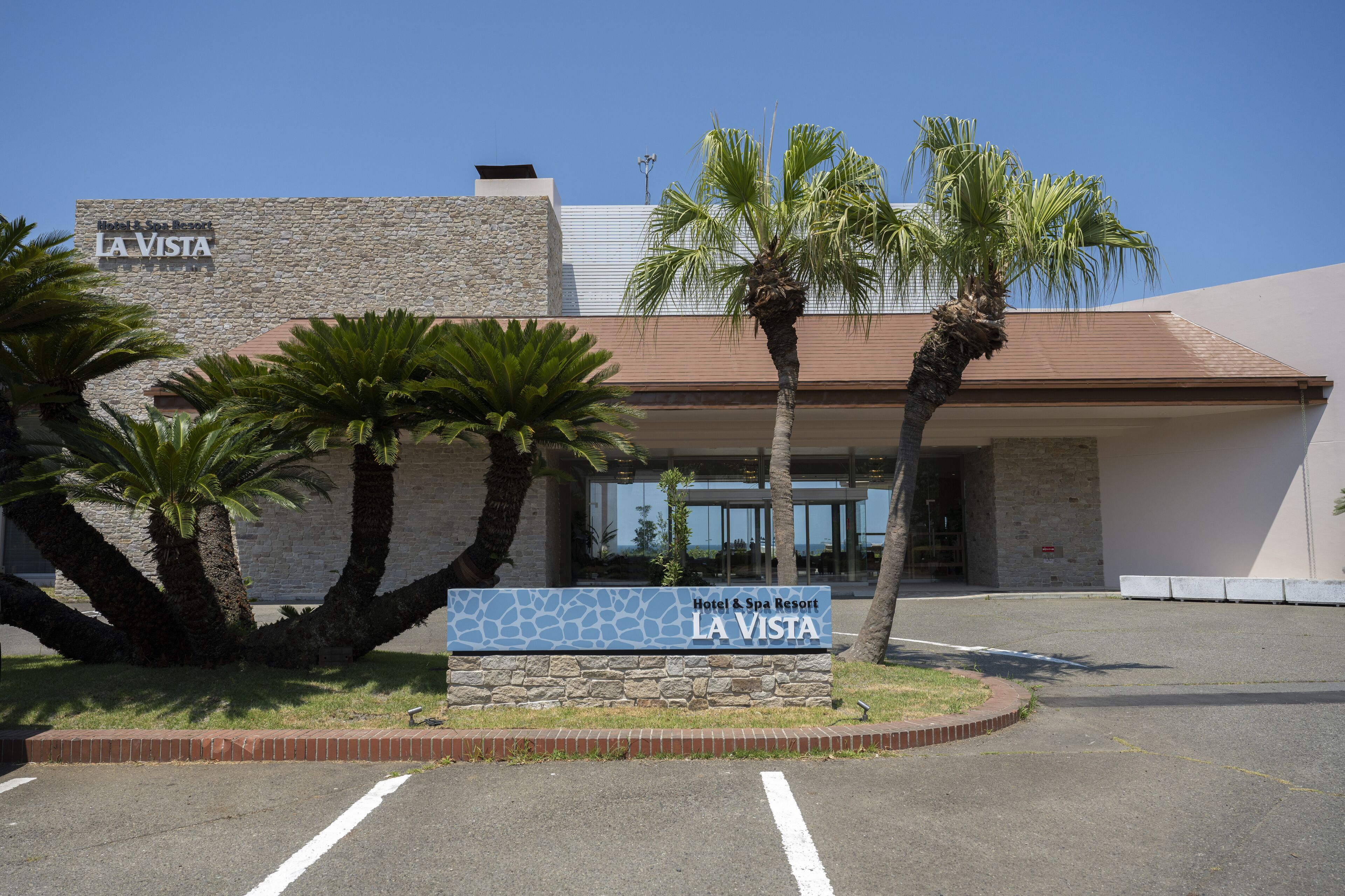 A hotel entrance with a sign reading "Hotel & Spa Resort LA VISTA" and palm trees in the foreground.