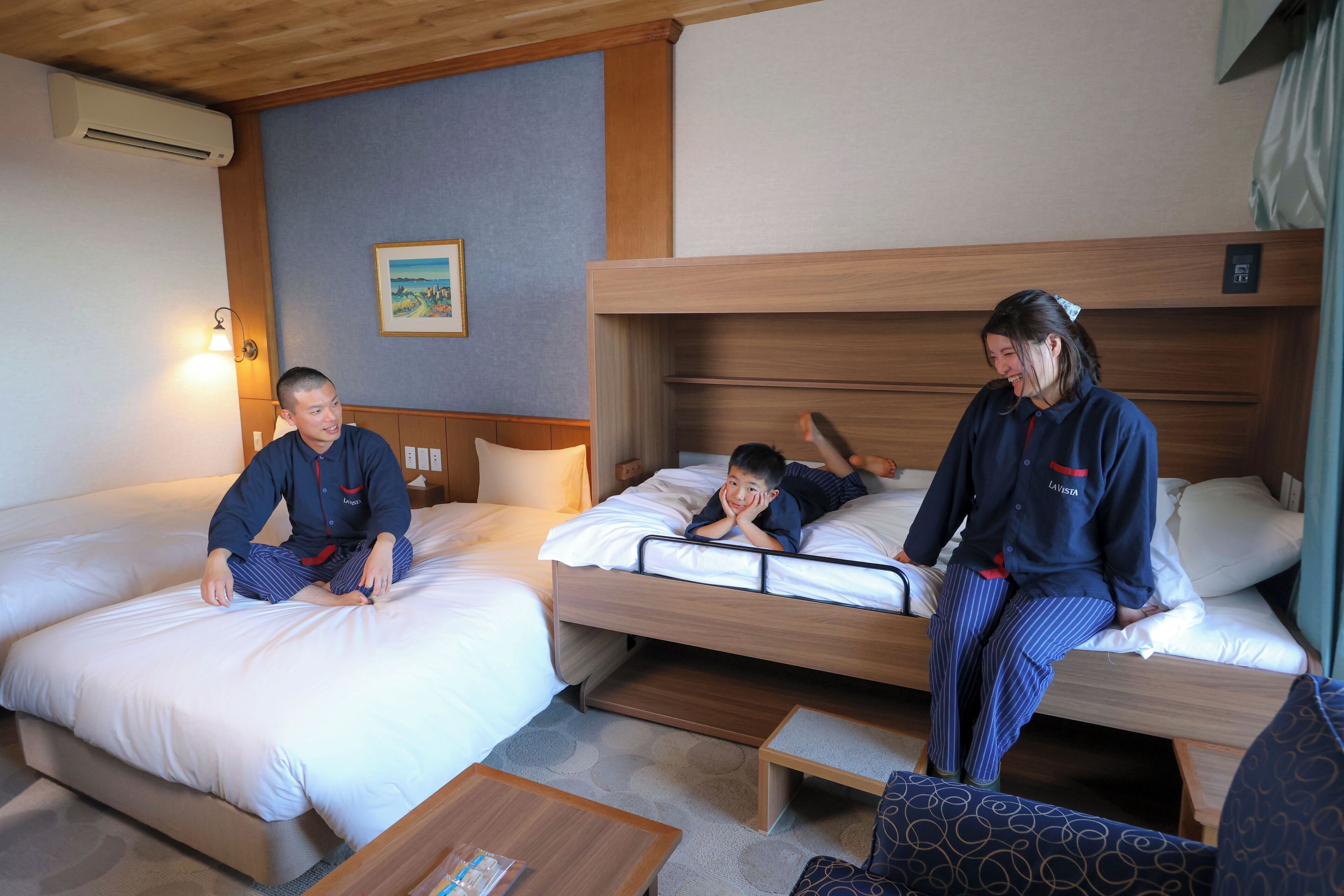 Quarto de hotel com duas camas, um sofá pequeno e teto de madeira.
