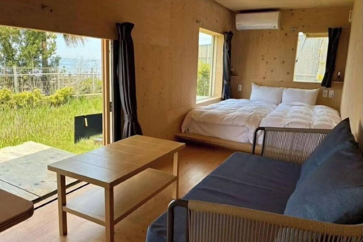 Habitació amb llit, sofà, taula i finestra que donen a una zona verda.