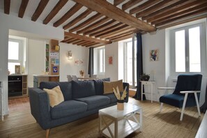 Una sala de estar con un sofá, una mesa de centro y una silla. Se observa un área de cocina al fondo.