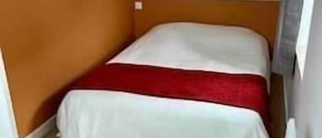 A small, single-bed room with a sloped ceiling, wooden flooring, and a red bedspread.