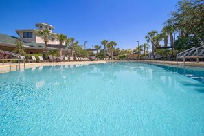 A clear blue pool with lounge chairs and palm trees around.