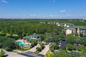 A resort with multiple buildings, a swimming pool, and a parking area surrounded by greenery.