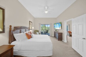 A hotel room with a large bed, a ceiling fan, a TV, and a balcony with outdoor seating.