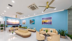 A modern hotel lobby with a blue accent wall, a reception desk, comfortable seating areas, and artwork. - The Home Hotel & Apartment (Da Nang)