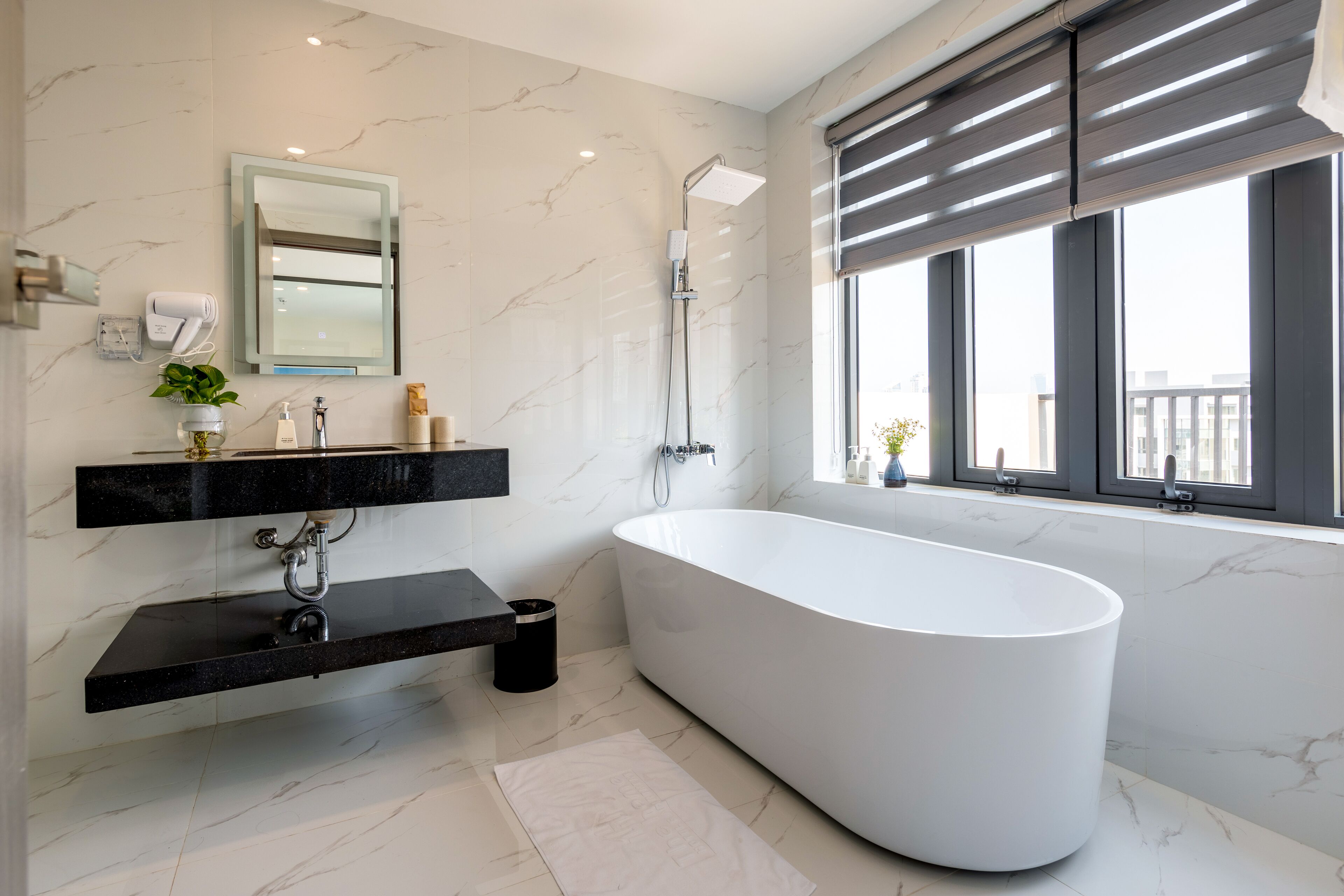 Une salle de bain moderne avec une baignoire sur pieds, un grand miroir et une fenêtre avec des stores.