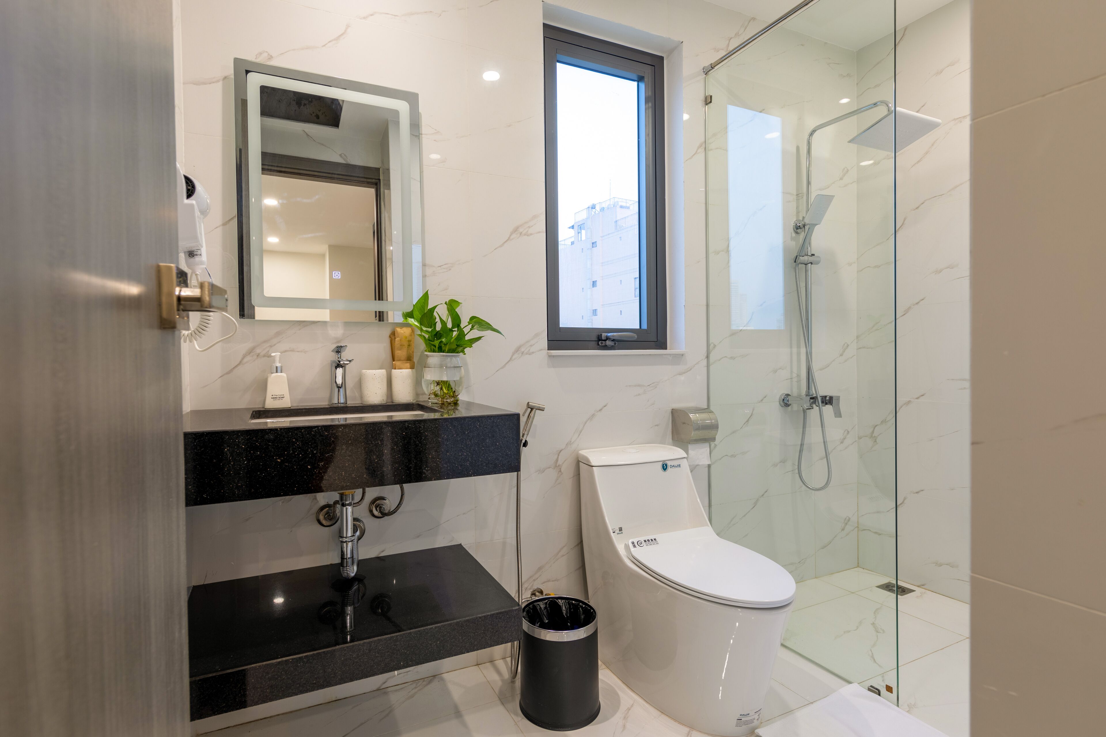 A modern bathroom with a black countertop, a white toilet, a glass-enclosed shower, and a window providing natural light.