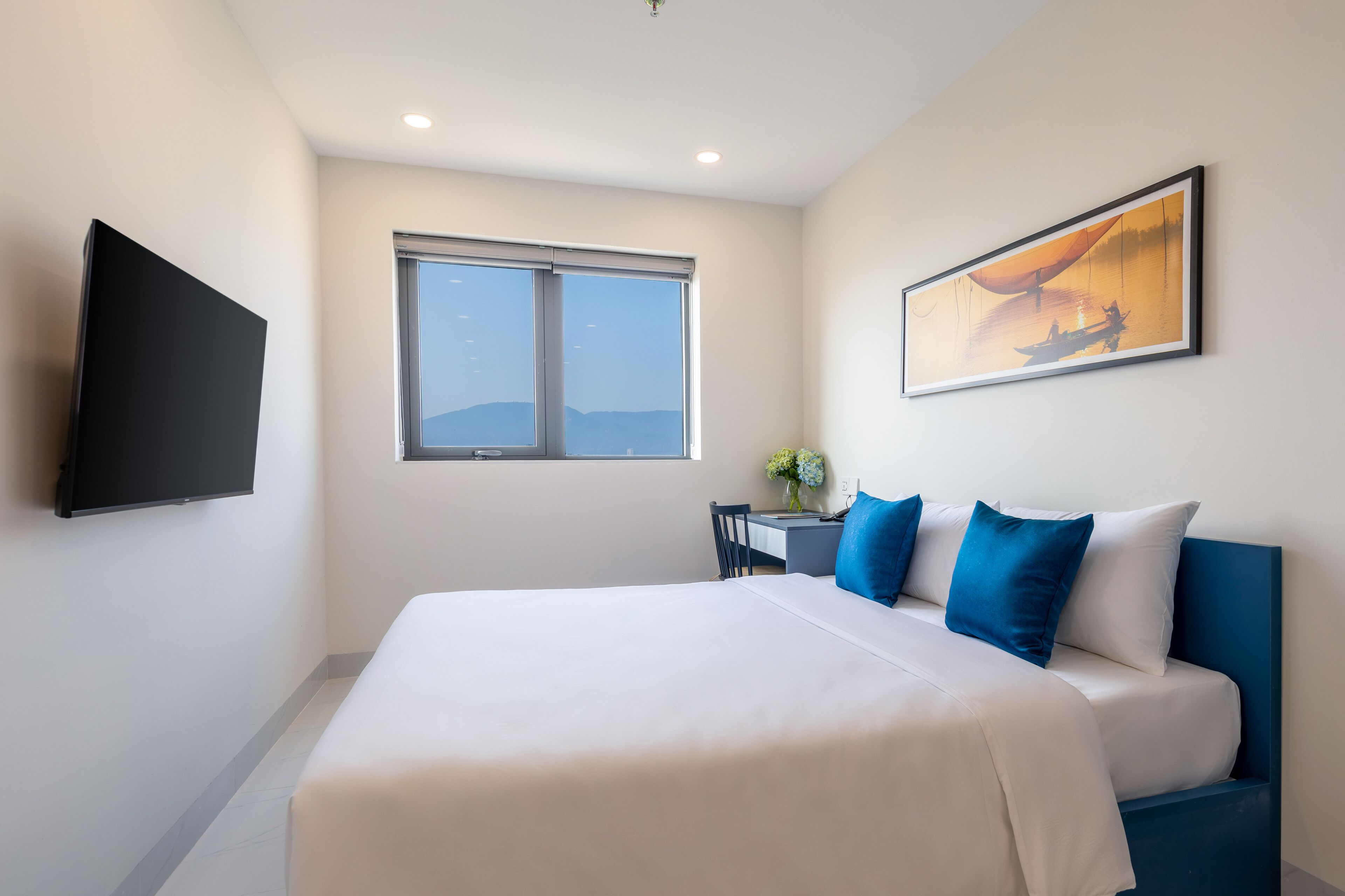 Hotelkamer met een groot bed, een flatscreen-tv, een bureau met stoel en een raam met uitzicht op de bergen.