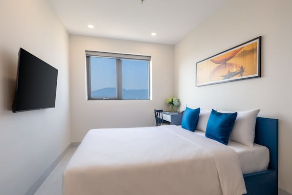 Una habitación de hotel con una cama grande, un televisor de pantalla plana, un escritorio con una silla y una ventana con vistas a las montañas.
