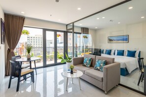 Una habitación de hotel moderna con sofá, mesa de comedor, pequeña mesa de centro y cama con ropa de cama azul y blanca.