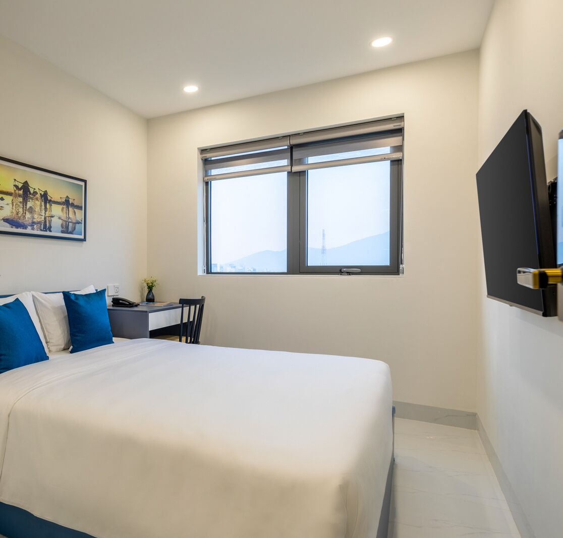 Une chambre d’hôtel avec un grand lit, un bureau, une chaise, une télévision et une fenêtre avec des stores.