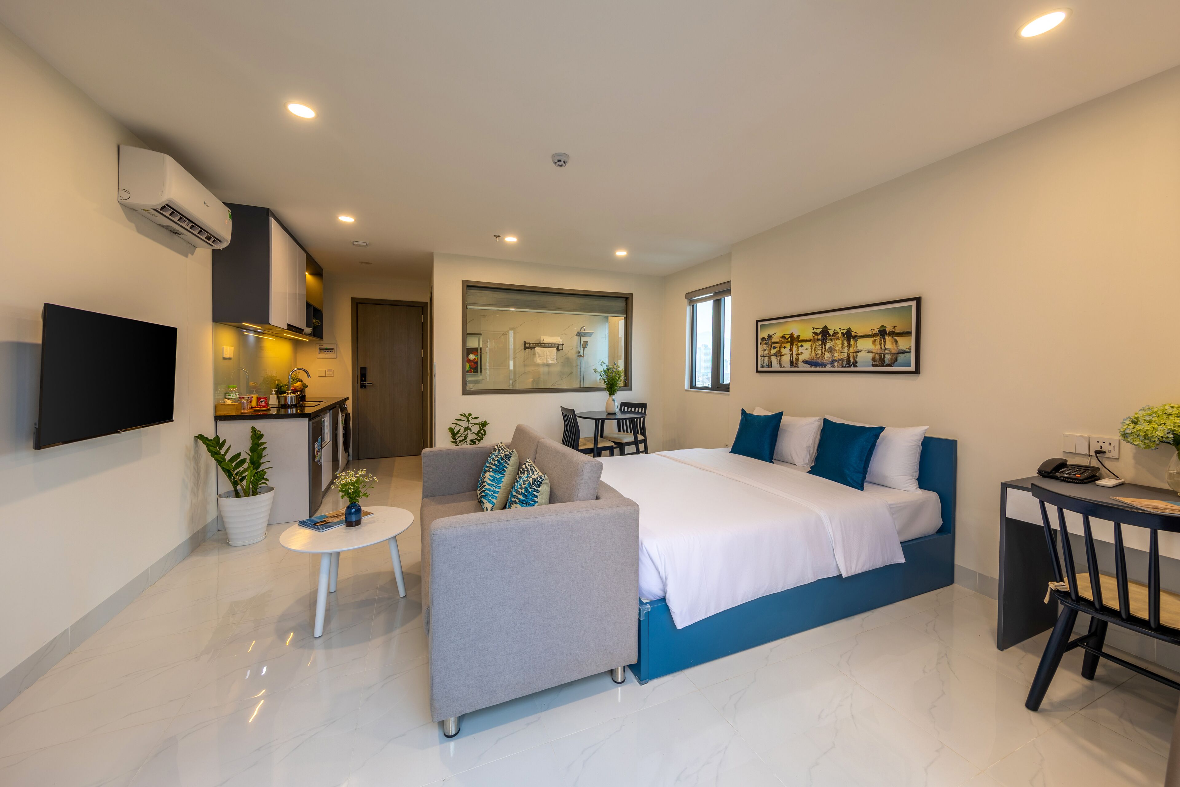 Une chambre d’hôtel moderne équipée d’un lit, d’un canapé, d’une petite table, d’une télévision et d’une kitchenette.