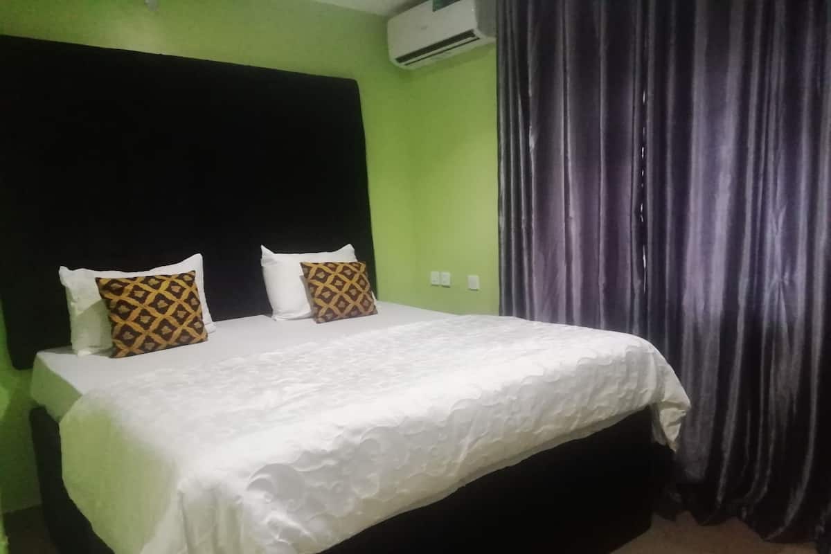 A bed with white bedding and two patterned pillows, a black headboard, and a green wall.