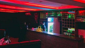 Een bar met een toonbank, flessenkasten en een koelkast.