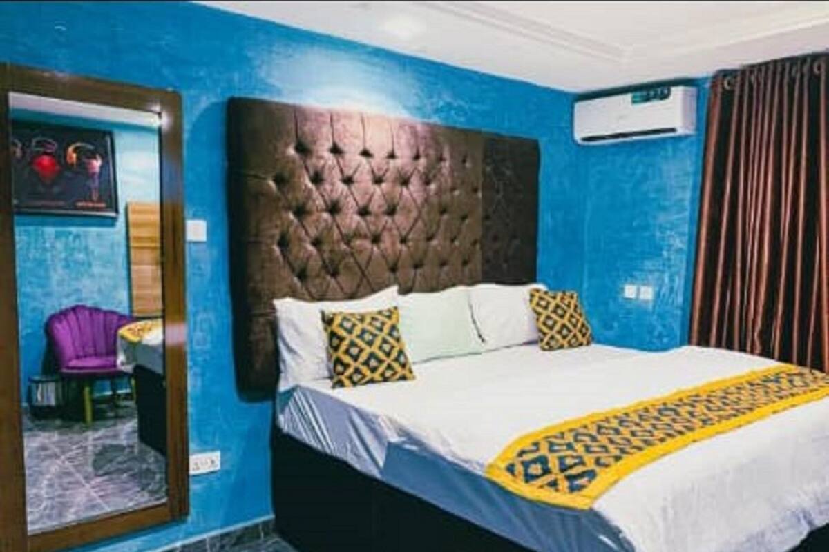 A bedroom with a tufted headboard, a bed with patterned bedding, a chair, and an air conditioning unit.