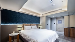 A modern hotel room with a large bed, a small bedside table, a wall-mounted light, and a door with a sign. - modayhotel (Taichung)