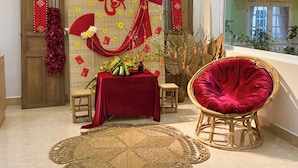 Ein Zimmer mit traditioneller chinesischer Dekoration, ein roter Tisch mit Geschenken, ein Korbstuhl und ein großes Fenster.