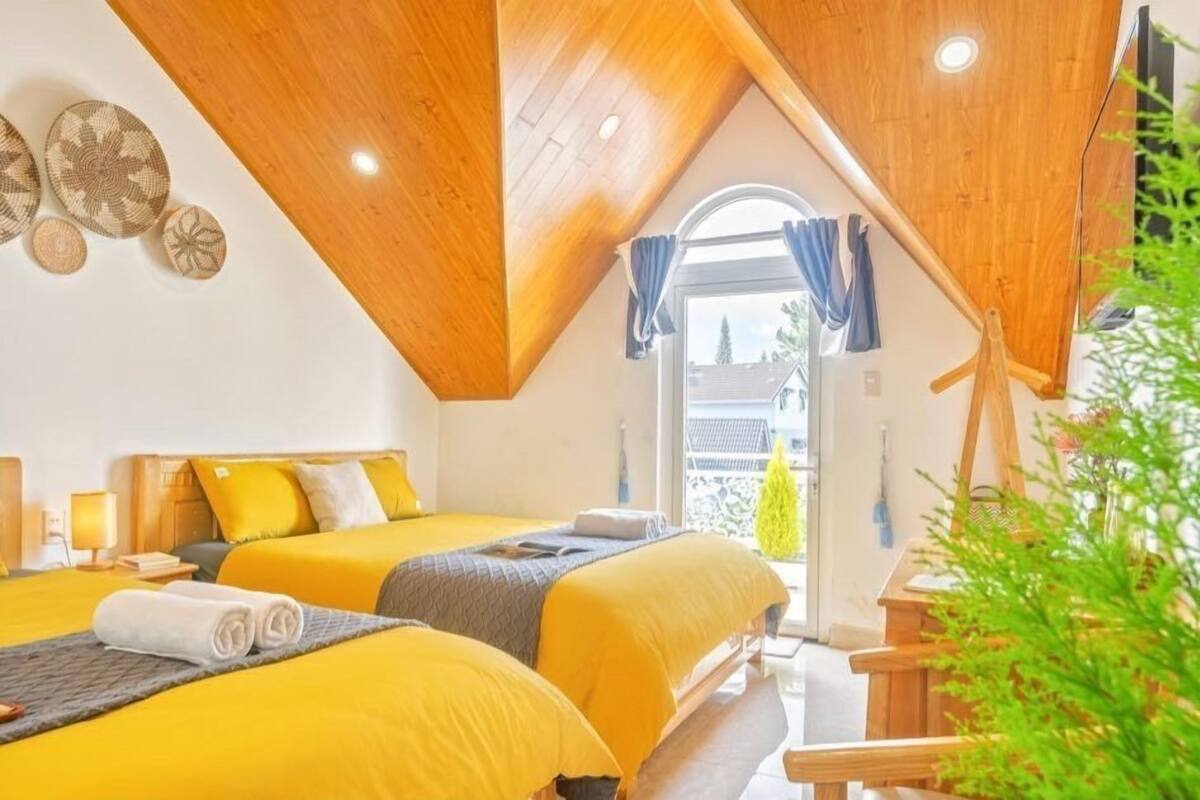A bedroom with two beds, wooden ceiling beams, a window with curtains, and a view of the outside.