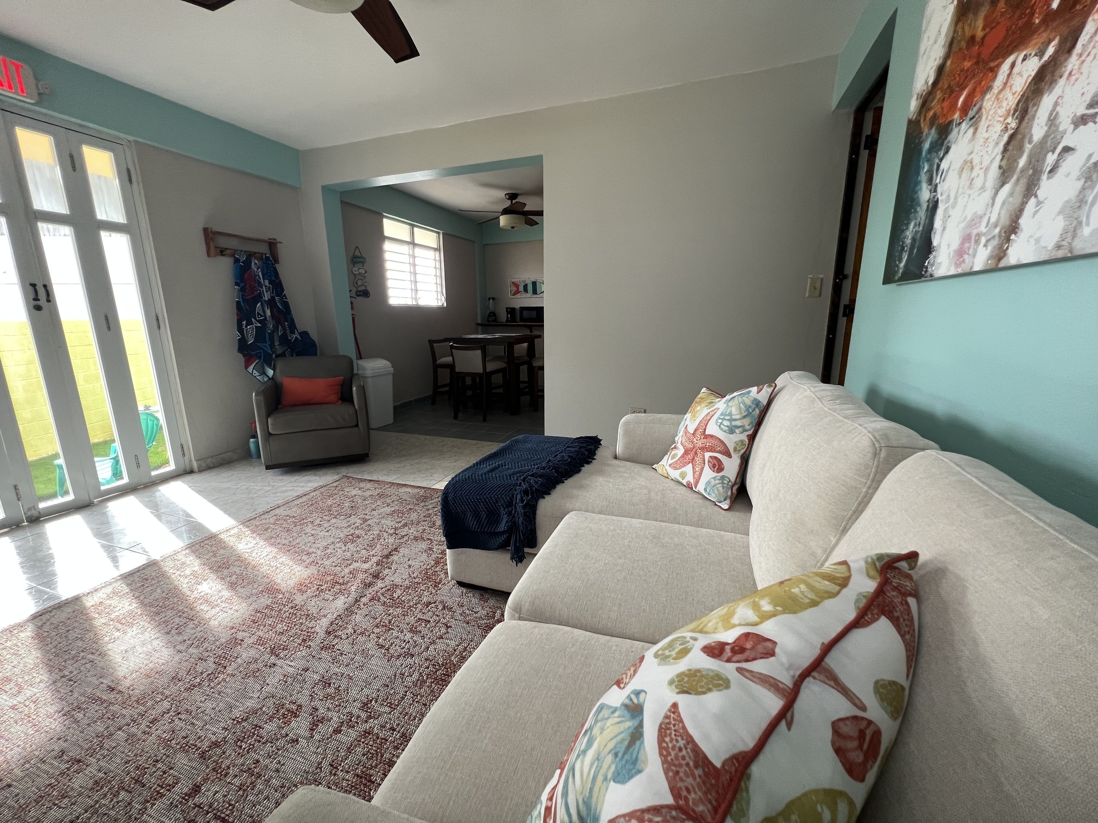 A living room with a sofa, a patterned rug, and a dining area in the background.
