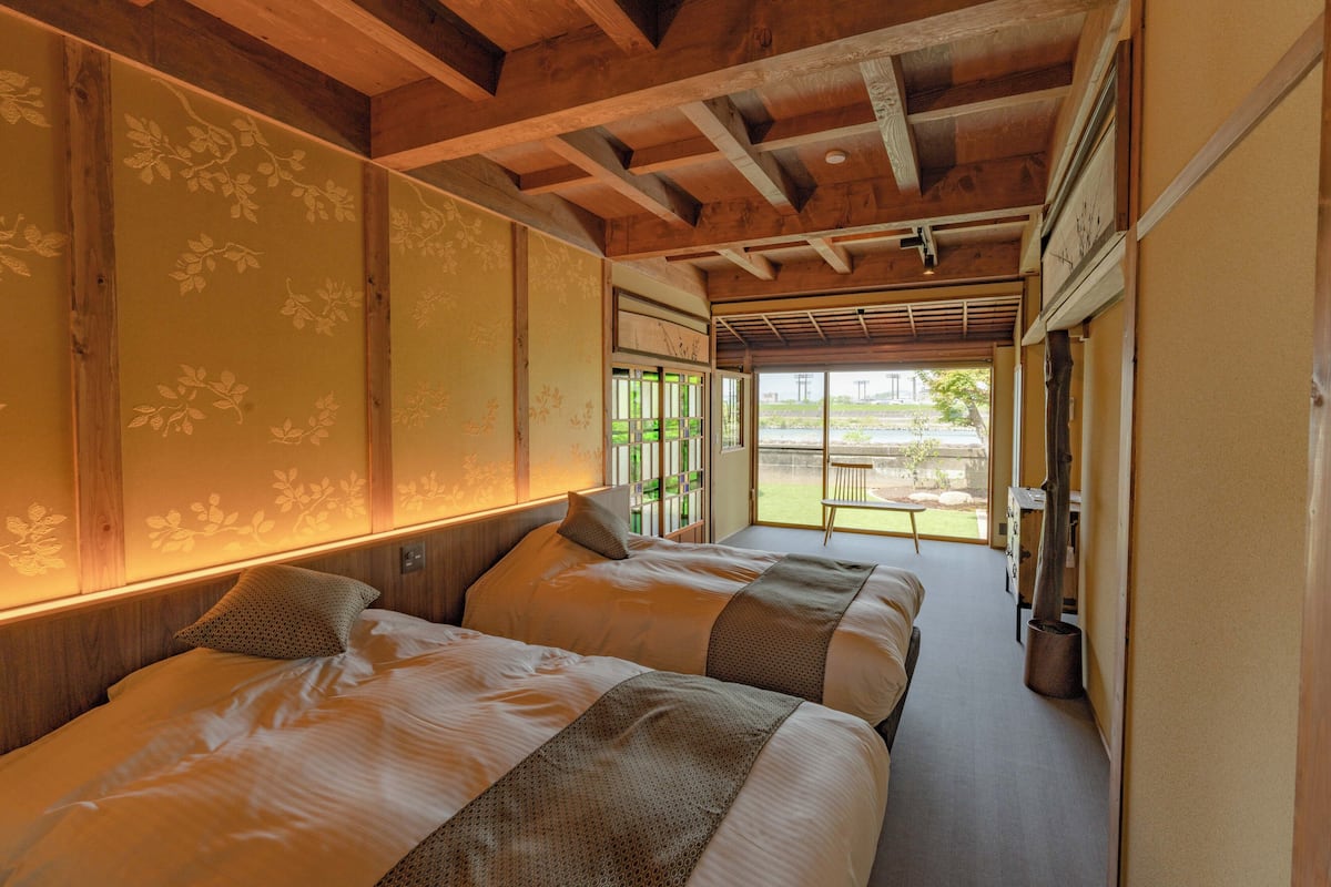 Ein Hotelzimmer mit zwei Betten, Holzbalken an der Decke und Blick ins Freie.