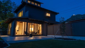 Een modern herenhuis met twee verdiepingen, een grote glazen voordeur, een terras met tuinmeubilair en een verzorgd gazon.