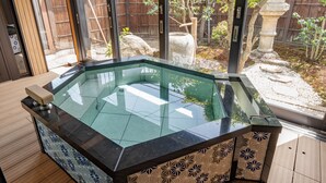 A modern hot tub with a glass top, surrounded by wooden flooring and patterned tiles.