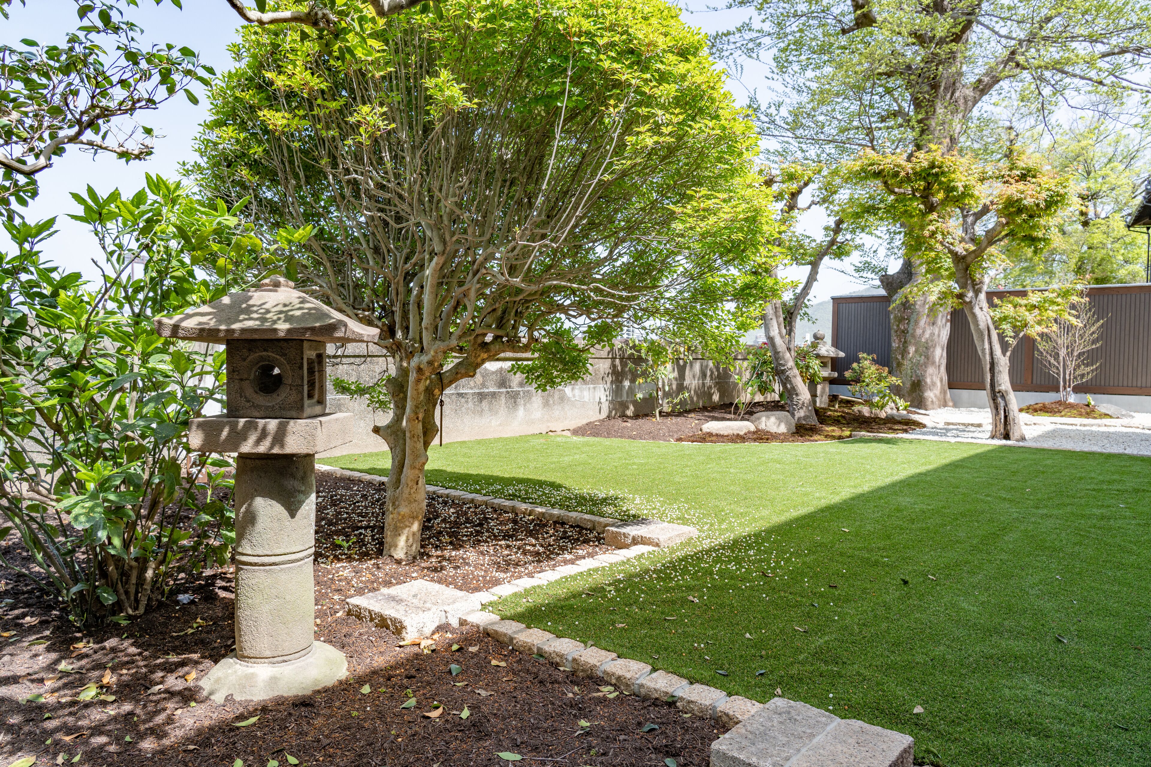 A well-maintained garden with a stone birdbath, neatly trimmed grass, and mature trees.
