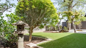 A well-maintained garden with a stone birdbath, neatly trimmed grass, and mature trees.
