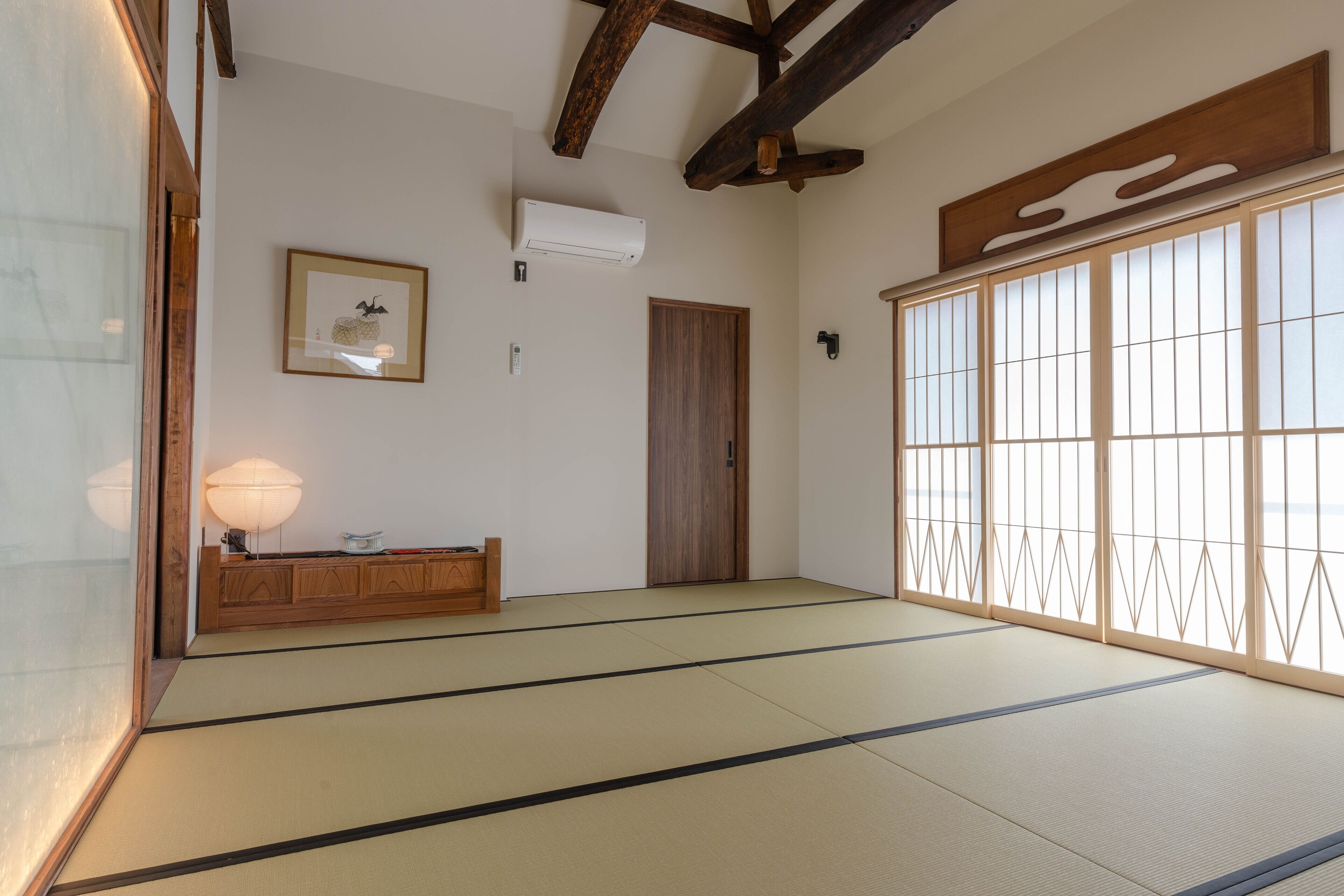A traditional Japanese room with tatami flooring, a wooden cabinet, a sliding door, and a framed picture on the wall.