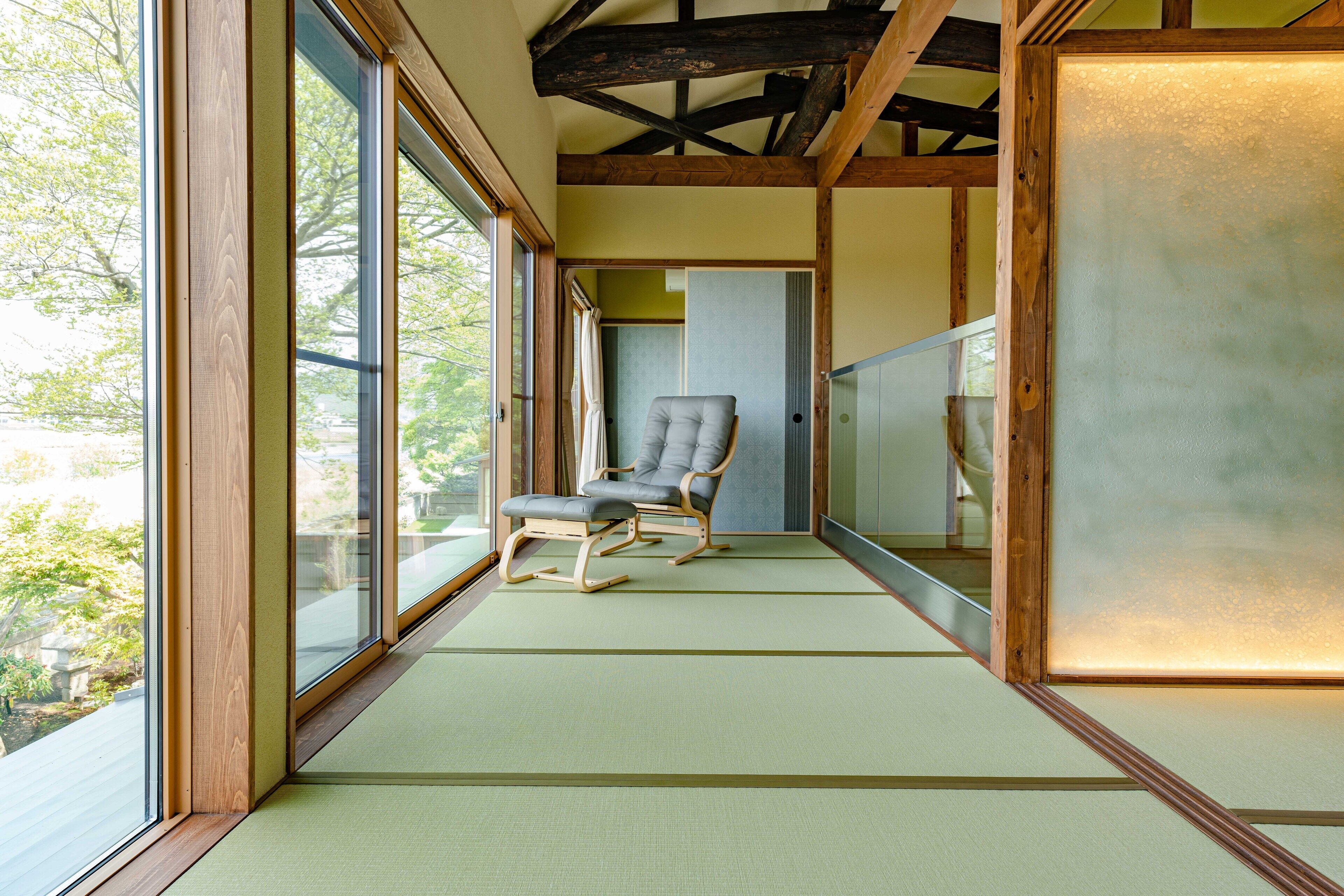 A corridor with a tatami mat floor, a cushioned chair, and large windows.