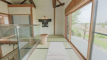 Um quarto japonês tradicional com piso de tatame, um painel shoji e vista para o exterior.