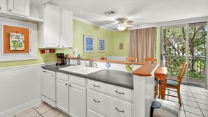 A kitchen with white cabinets, a black countertop, and a dining area with a table and chairs. - Villa 260 Getty Building (Jekyll Island)