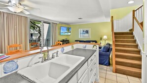 A kitchen with a large island, a dining area with chairs, a sofa, and a staircase. - Villa 260 Getty Building (Jekyll Island)