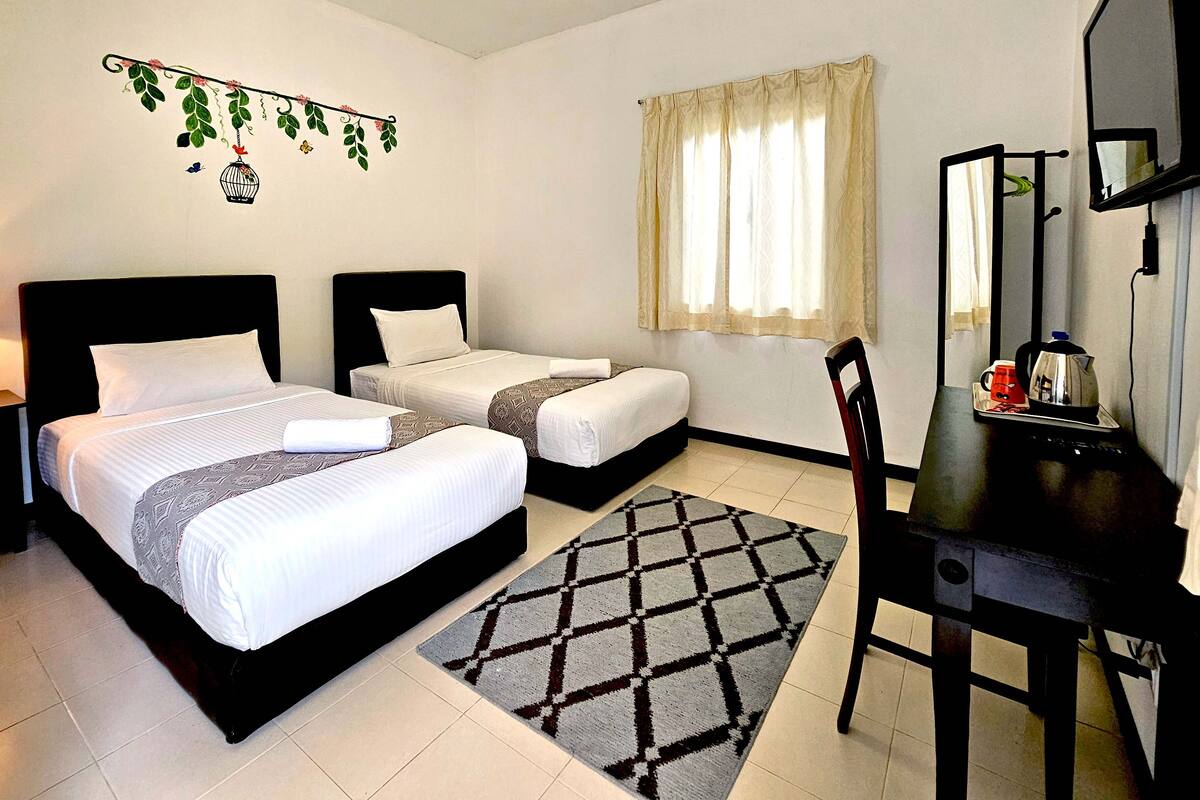 Une chambre d’hôtel avec deux lits, un bureau avec une chaise, un miroir et une fenêtre avec des rideaux.