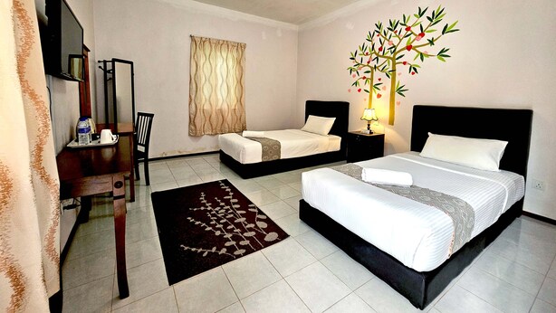 Une chambre d’hôtel comprenant un lit, un bureau avec une chaise, une petite table avec une bouteille et des verres, une fenêtre avec des rideaux et une décoration murale représentant un arbre orné de cœurs.