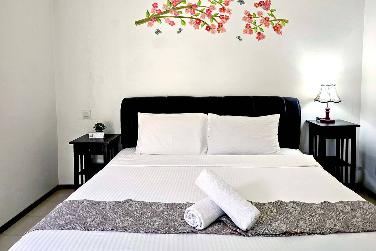 Un lit bien fait, avec du linge de lit blanc, une tête de lit sombre et une décoration murale florale.