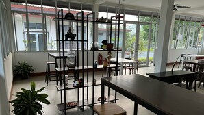Une pièce spacieuse dotée d’une grande fenêtre, d’une étagère en métal et d’un coin repas avec des tables et des chaises.