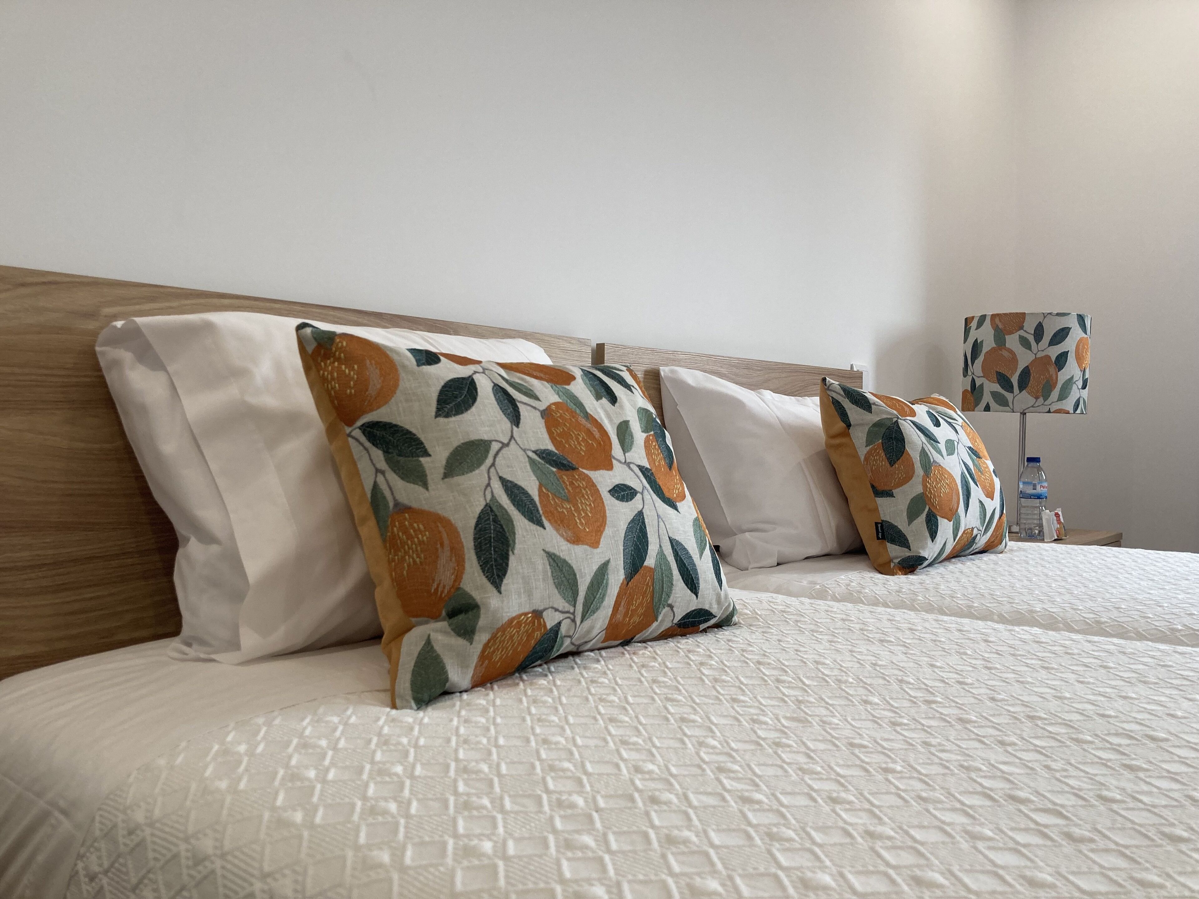 A hotel room with two beds, white bedding, and decorative pillows with an orange and green leaf pattern.