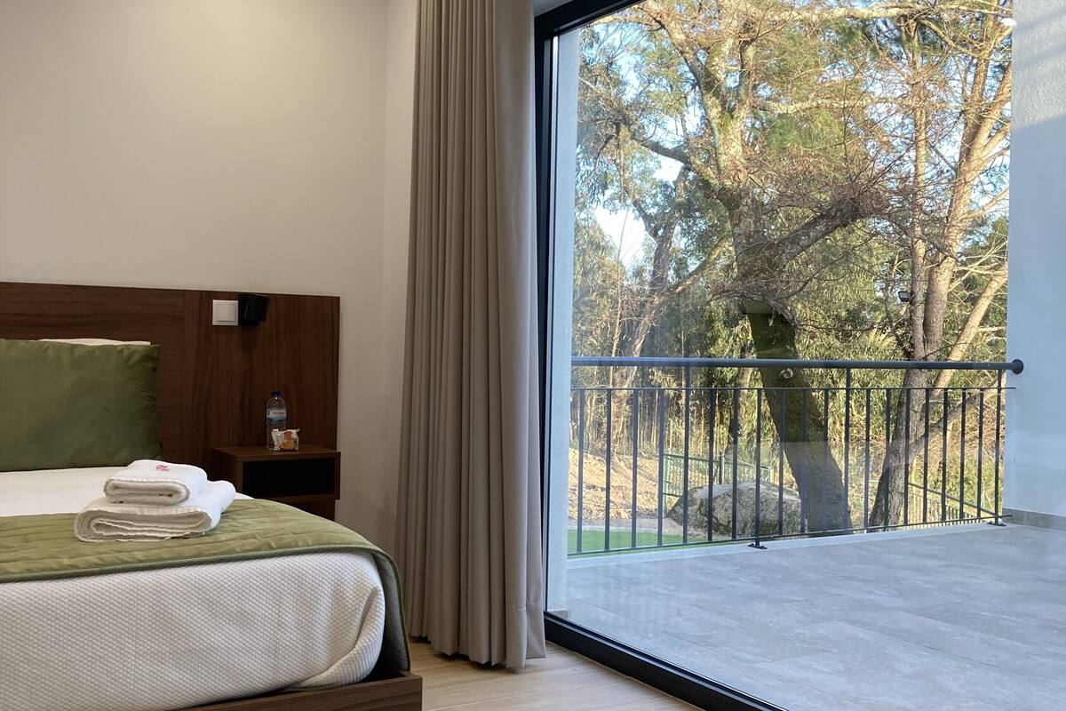 A modern bedroom with a large window, a wooden headboard, and a green rug.