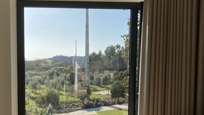 Une pièce dotée d’une grande porte-fenêtre coulissante donnant sur un balcon qui offre une vue sur un paysage verdoyant et un bâtiment situé au loin.