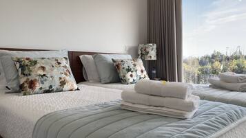 Habitación de hotel con dos camas, almohadas estampadas con motivos florales, una lámpara de noche y vistas a árboles a través de una ventana.